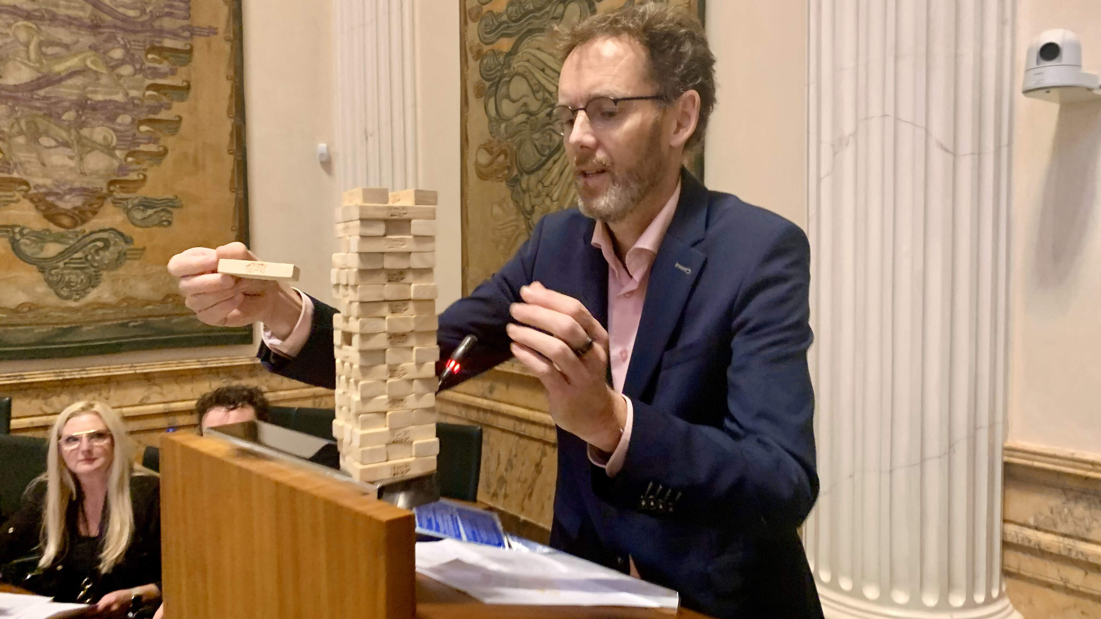 Michel Klein (ChristenUnie) voert op het spreekgestoelte een balanceeract uit met jenga-blokjes, om het provinciaal landschapsbeleid te illustreren.
